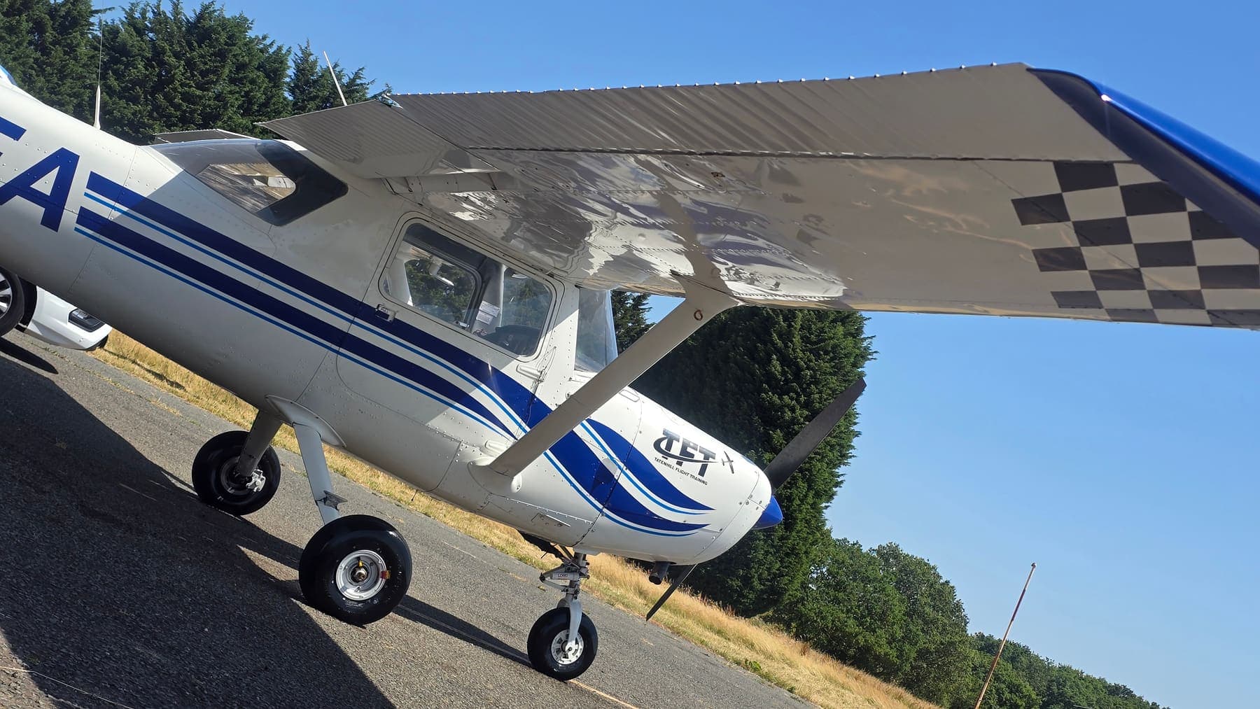 Under-wing view of a gleaming Cessna 152 after a fleet clean, checkerboard wingtip catching the sun